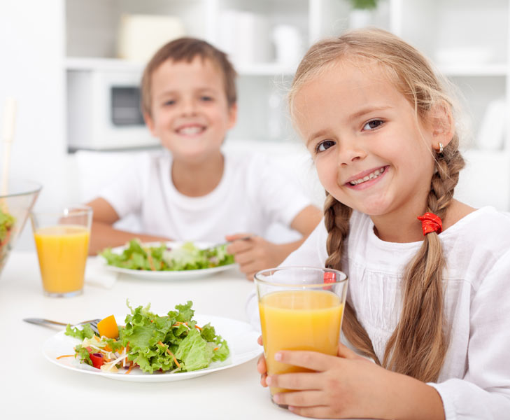 Ein Mädchen und Junge mit frischem Salat und einem Glas Orangensaft.