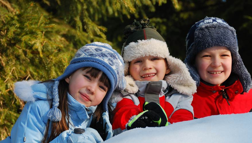 Drei Kinder mit Winterbekleidung freuen sich