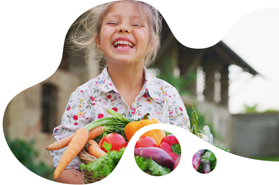 Ein Mädchen hält freudig lachend einen Erntekorb mit verschiedenem Gemüse.
